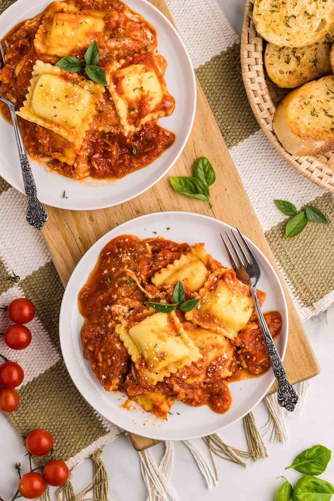 overhead view of two plates of ravioli lasagna, each on wooden cutting board with a fork, with basket of garlic bread on side