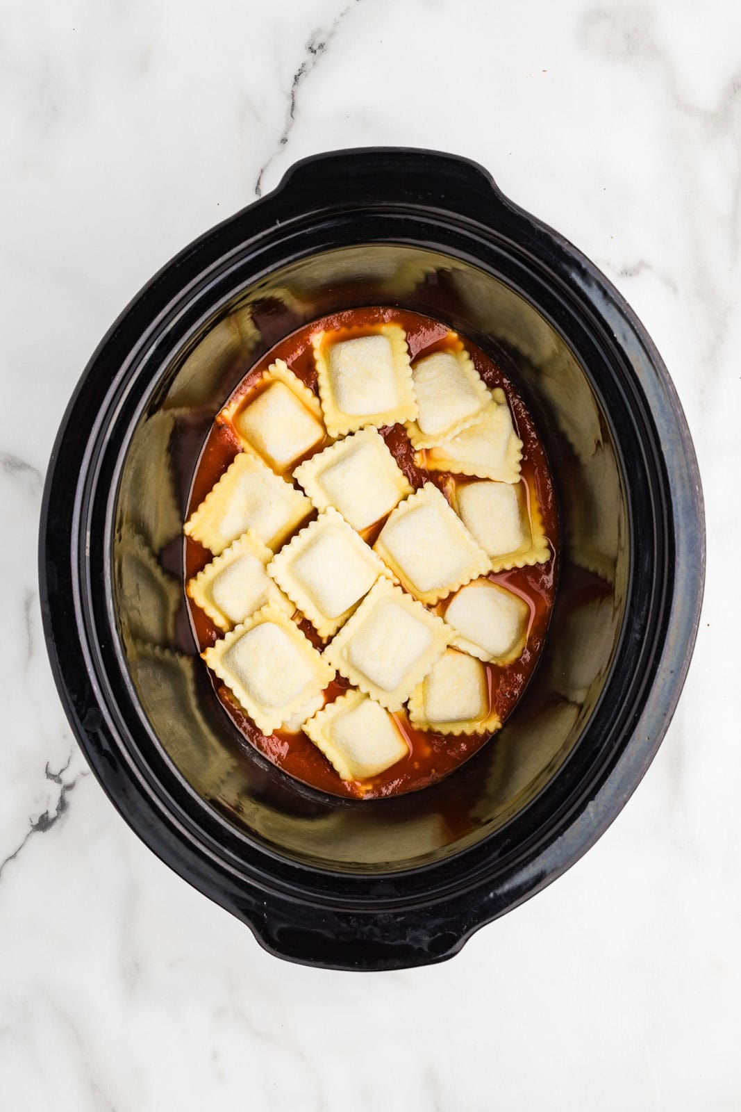 overhead view of black slow cooker with spaghetti sauce and ravioli