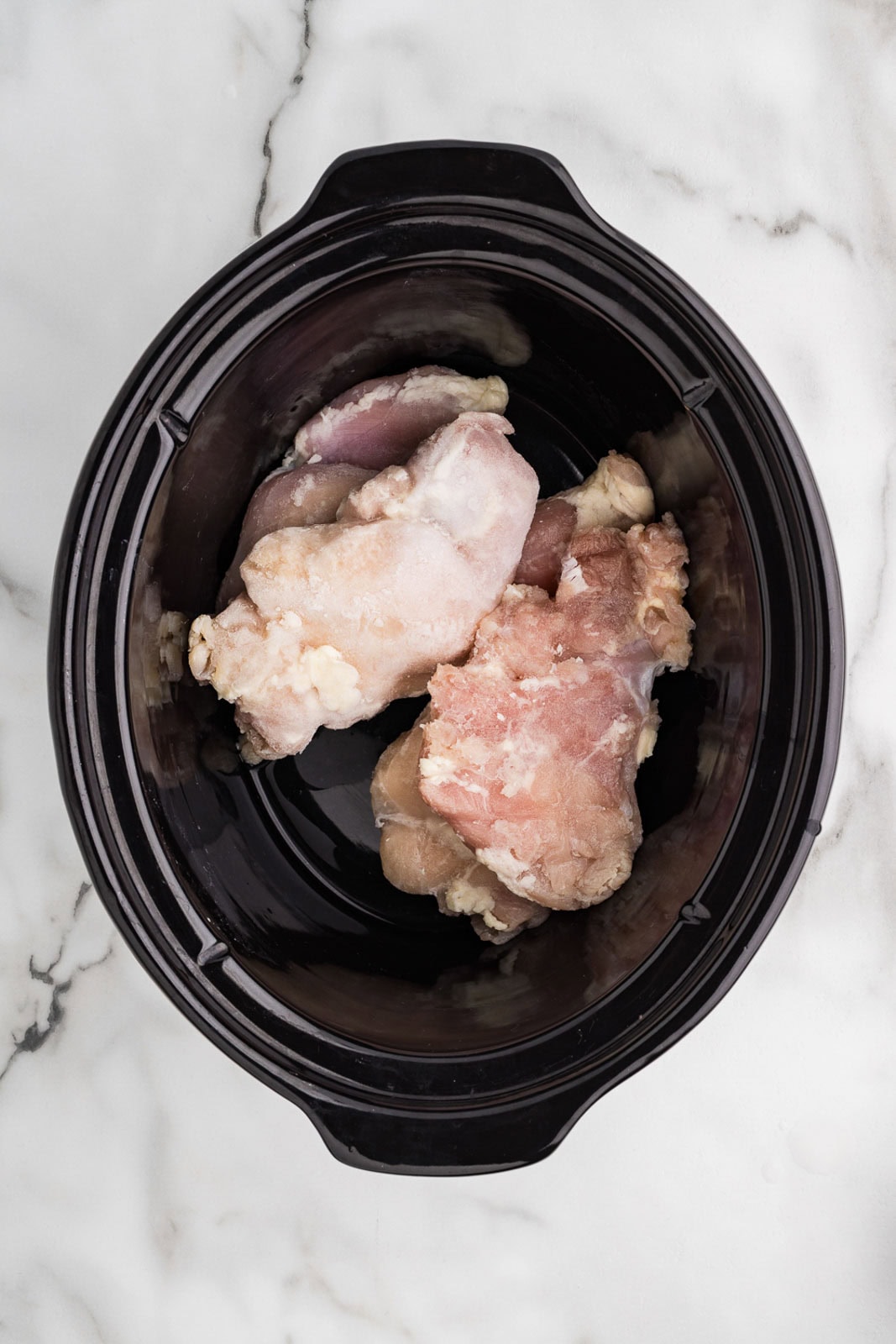 overhead view of chicken thighs in black slow cooker