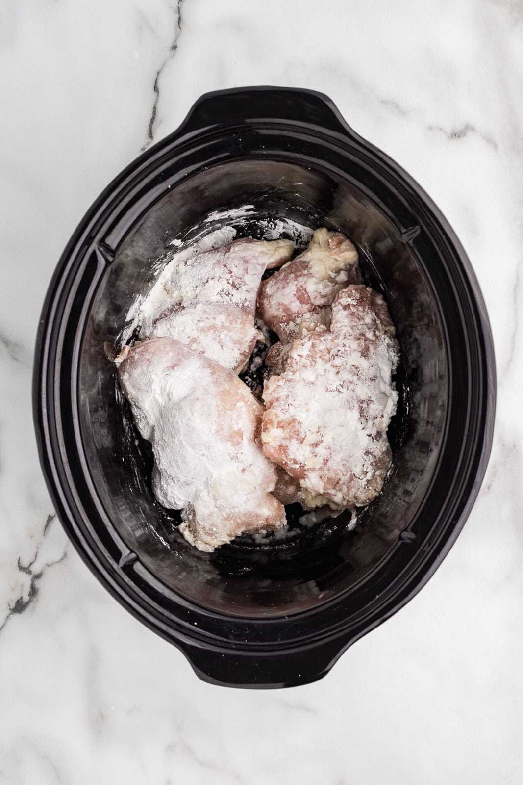 overhead view of chicken thighs in black slow cooker covered with cornstarch