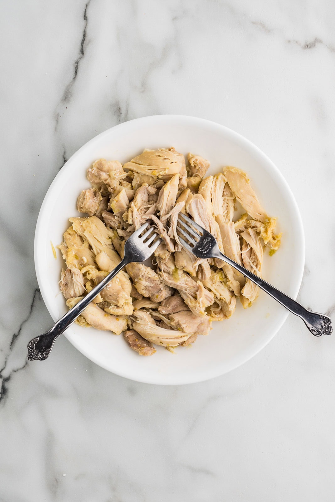 white plate with shredded chicken thighs and 2 forks