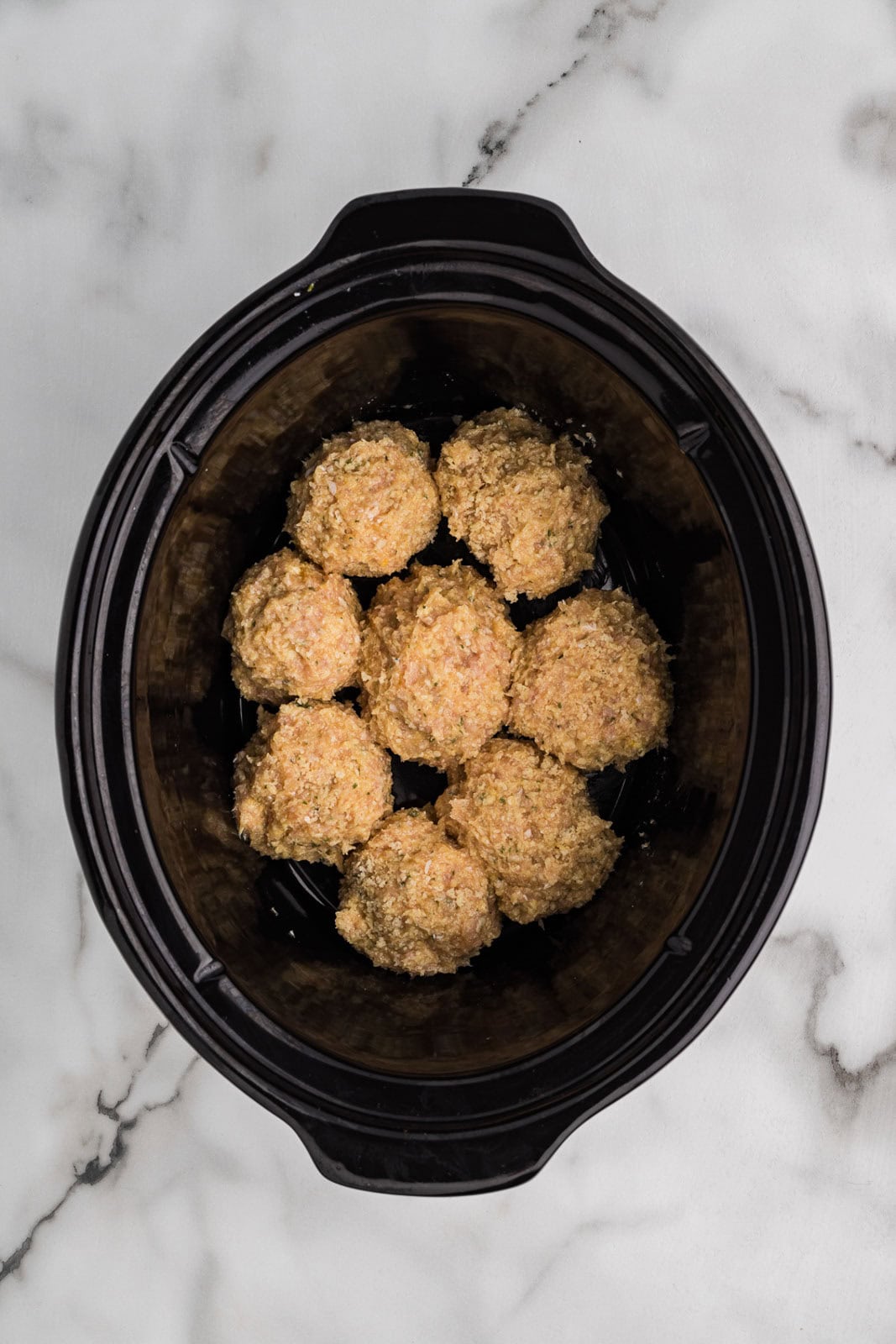 overhead view of black slow cooker with formed meatballs