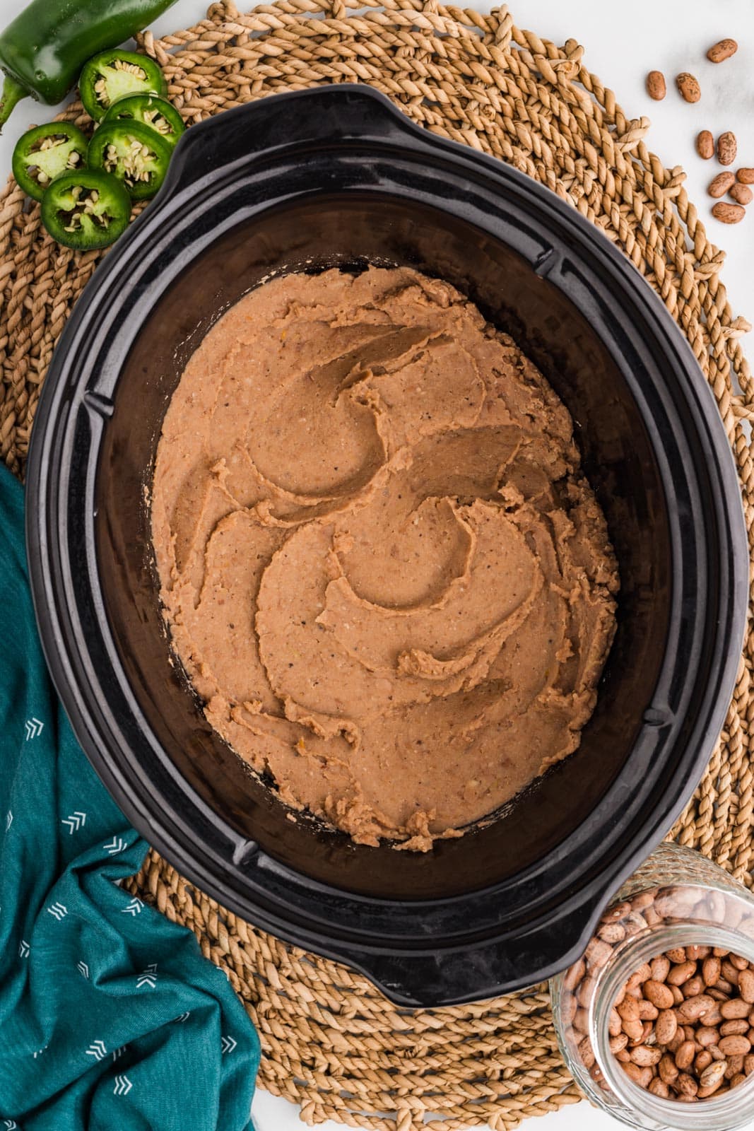 overhead view of black slow cooker of cooked refried beans on placemat