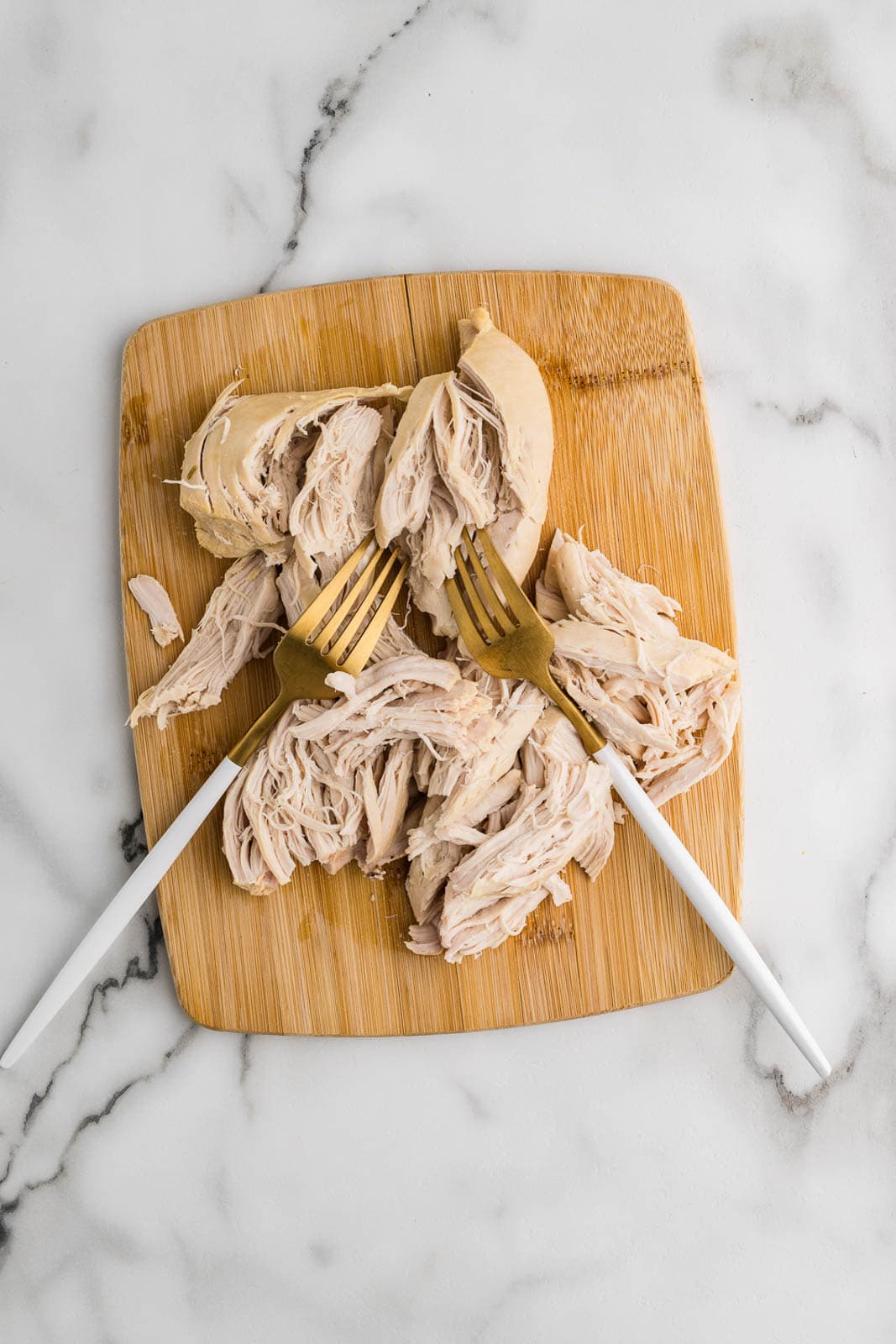 cutting board with shredded chicken with two forks