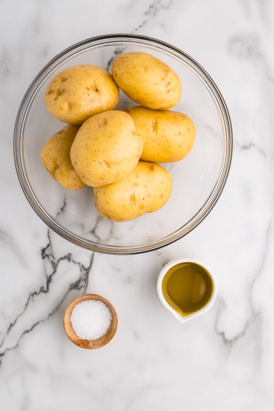 slow cooker baked potatoes ingredients to include large bowl of gold potatoes, wooden bowl of kosher salt, and small container of avocado oil