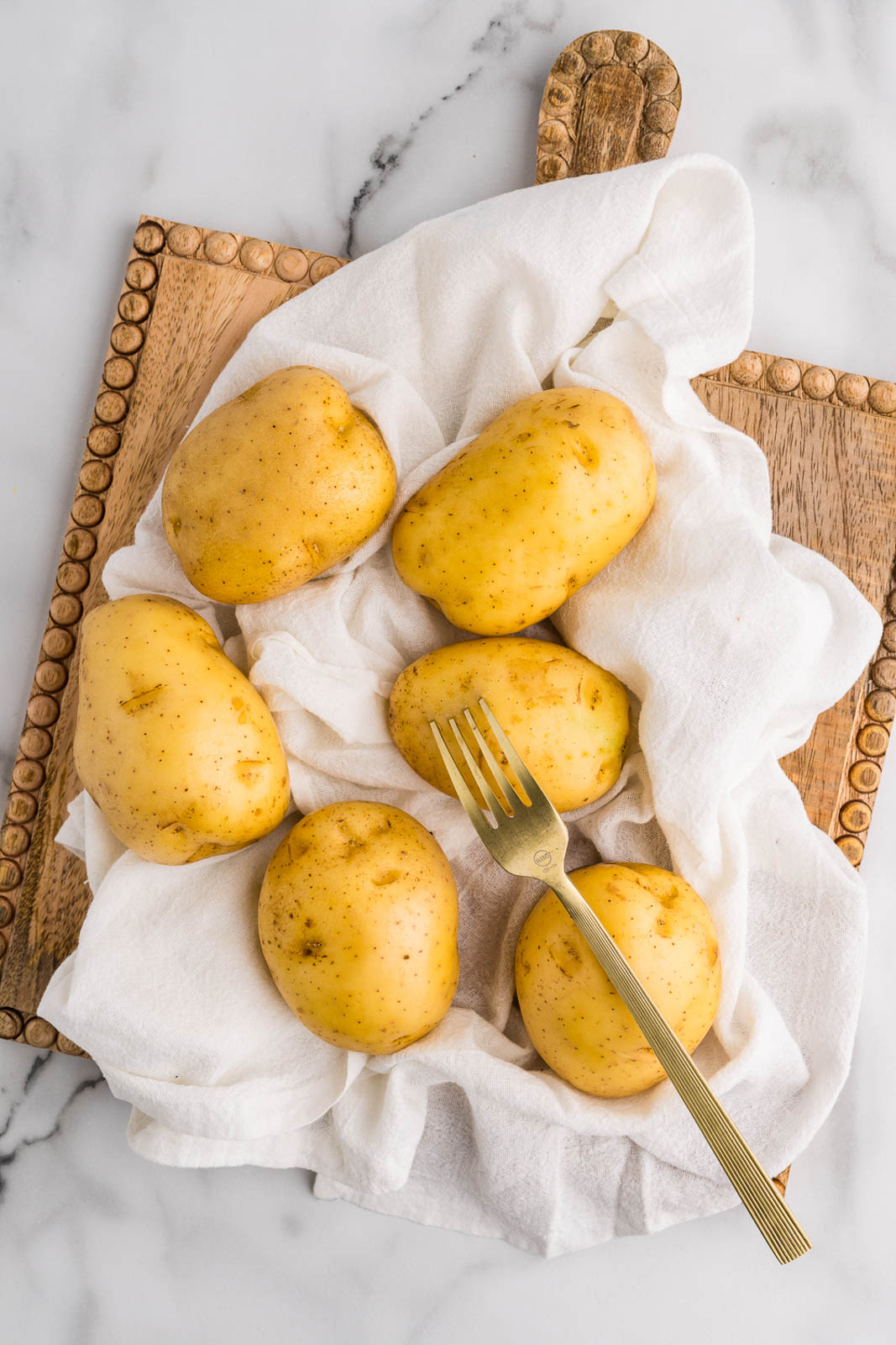 cutting board covered with white tea towel and six gold potatoes with gold fork