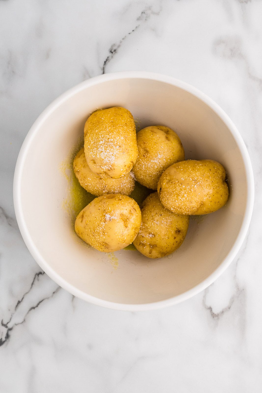 white bowl with six gold potatoes covered with oil and kosher salt
