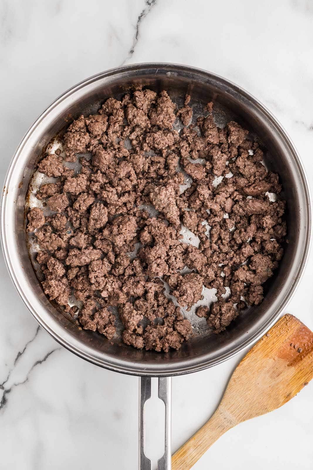 frying pan containing browned ground beef with a wooden spatula on the side