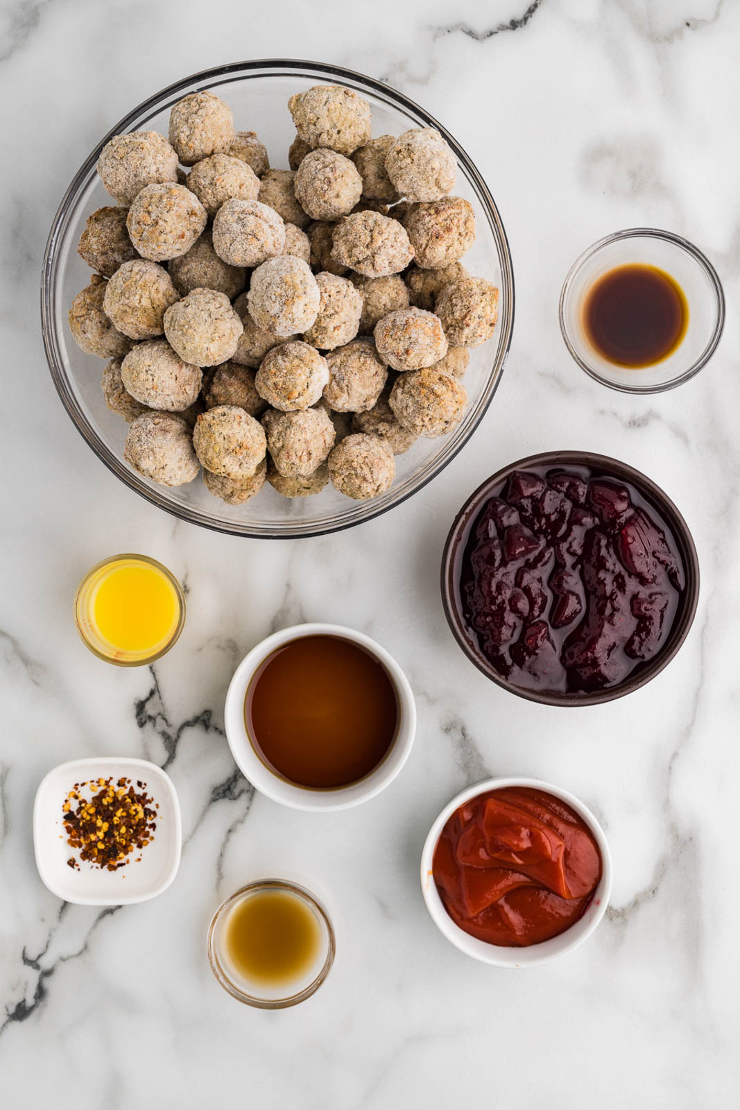 cranberry meatballs ingredients to include bowls containing frozen meatballs, cranberry sauce, ketchup, maple syrup orange juice, apple cider vinegar, Worcestershire sauce, and red pepper flakes