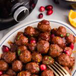 overhead view of white platter of meatballs with gold fork, with black slow cooker and bowl of rice in background