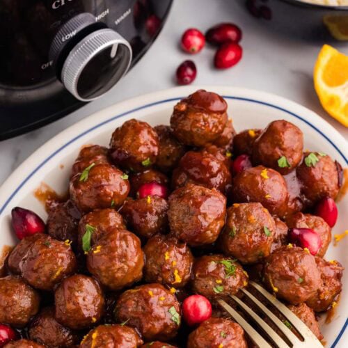 overhead view of white platter of meatballs with gold fork, with black slow cooker and bowl of rice in background