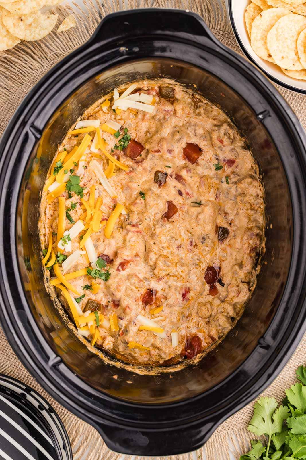 overhead view of slow cooked Rotel dip on placemat with bowl of chips on the side