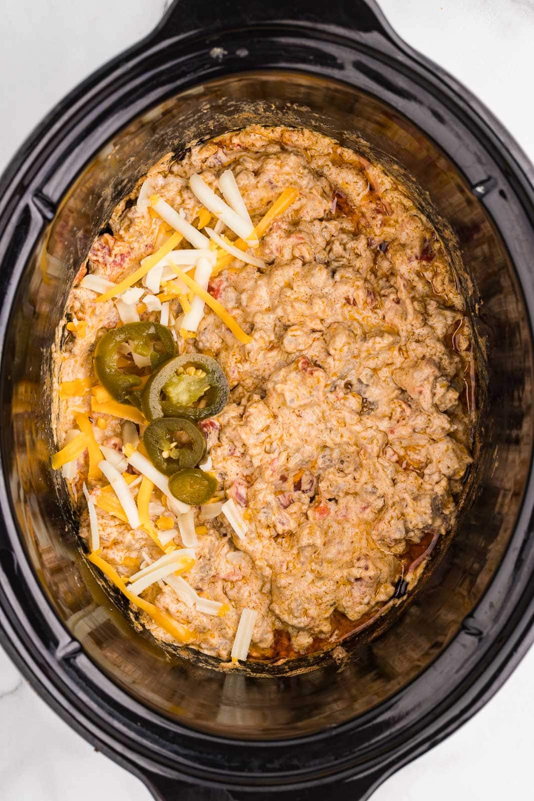 overhead view of black slow cooker containing cooked Rotel dip with jalapeno slices on top