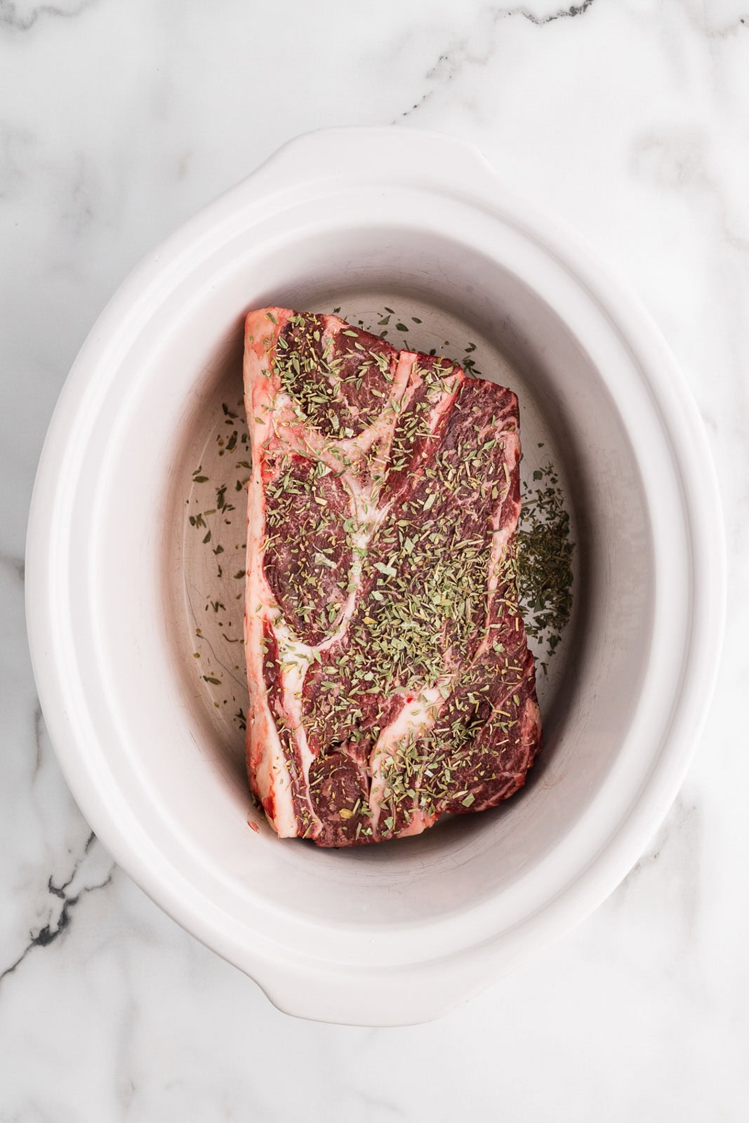 overhead view of white slow cooker with chuck roast and Italian seasoning