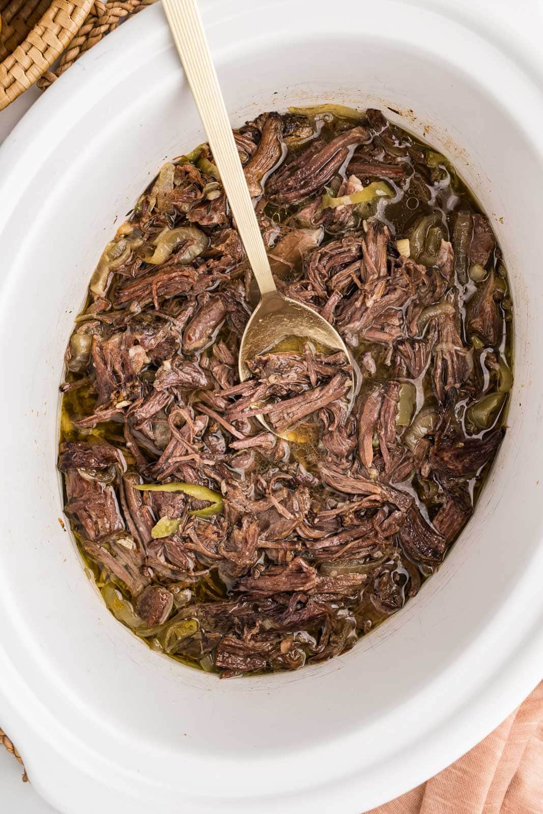 overhead side view of white slow cooker with slow cooked Italian beef with gold spoons