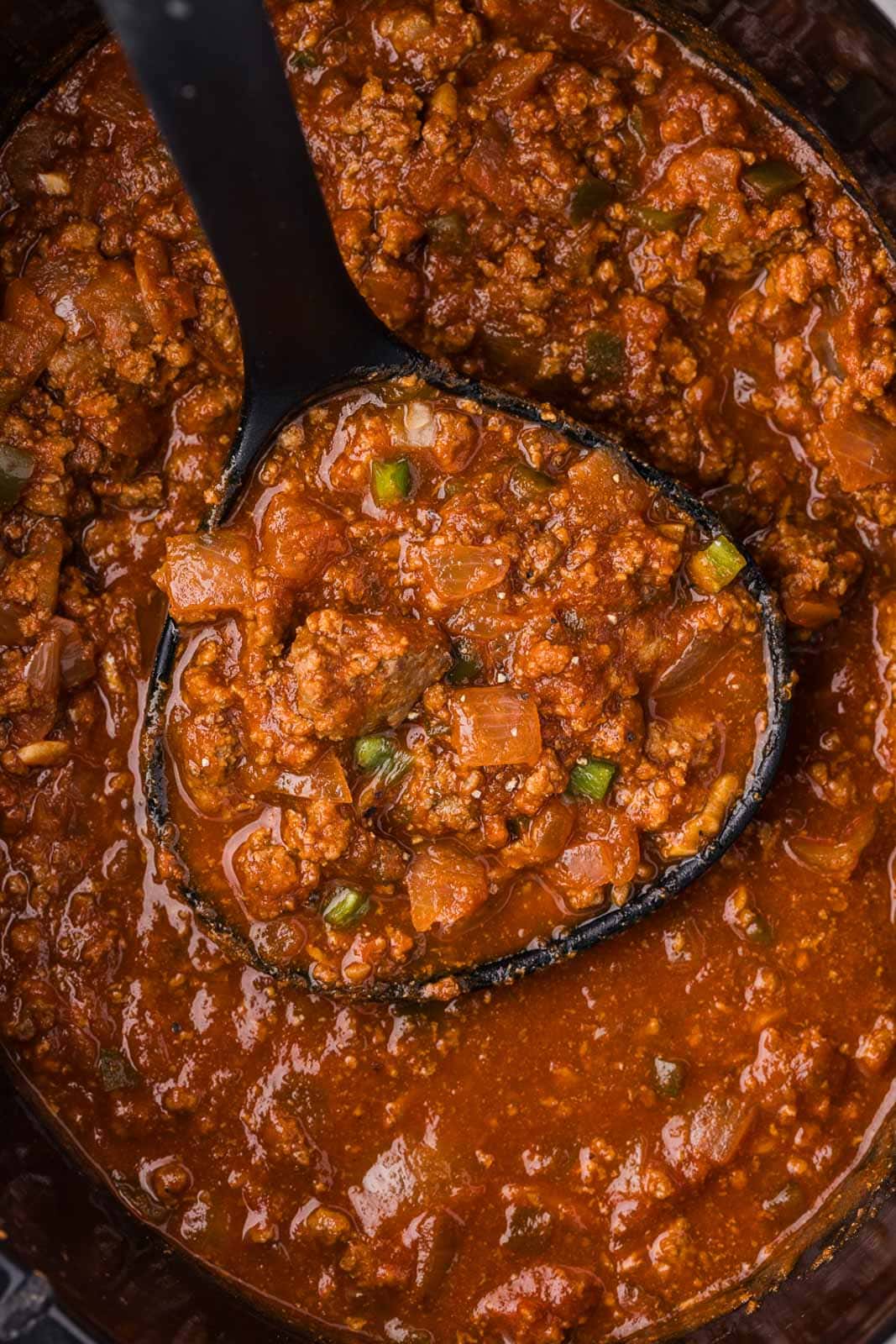 closeup view of chili in black slow cooker with black ladle
