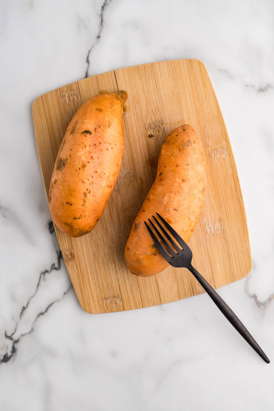wooden cutting board with two sweet potatoes and black fork