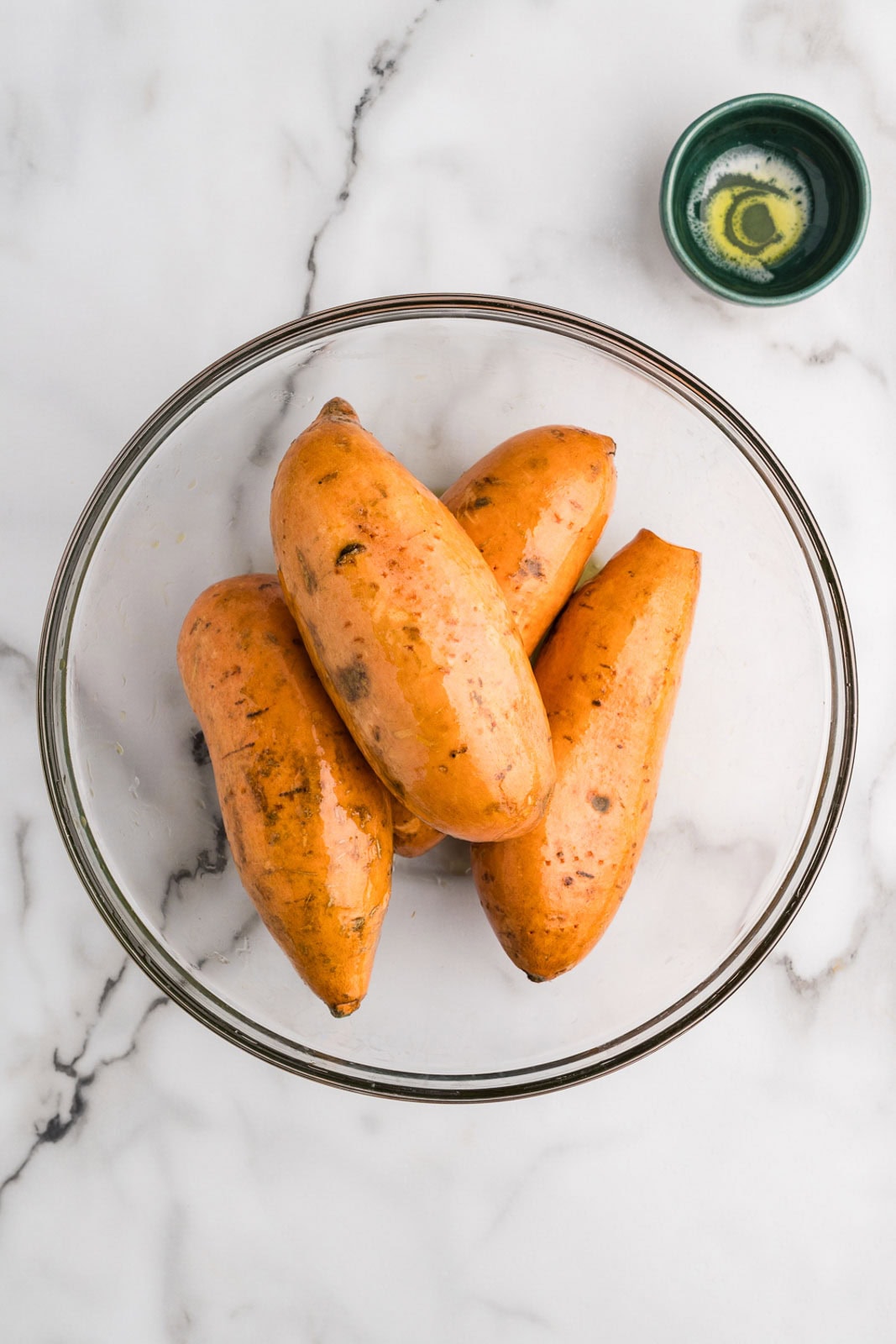 glass bowls with four pierced sweet potatoes and bowl of olive oil on side