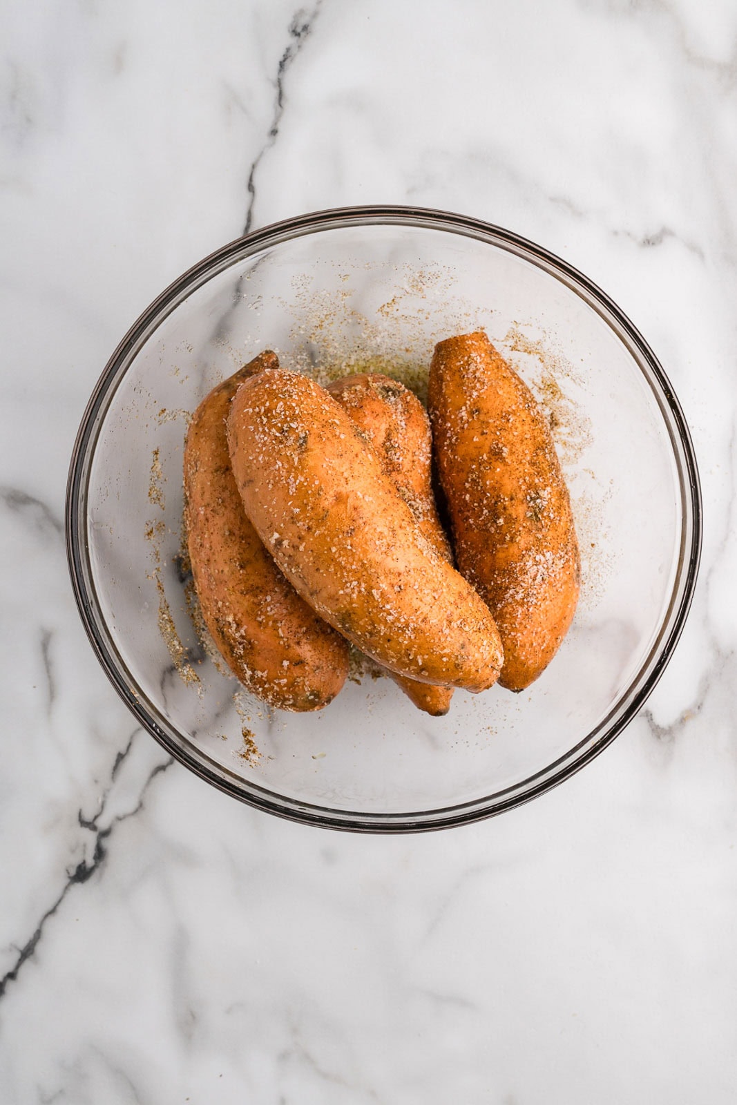 overhead view of sweet potatoes in clear glass bowl that have been rubbed with oil and spices