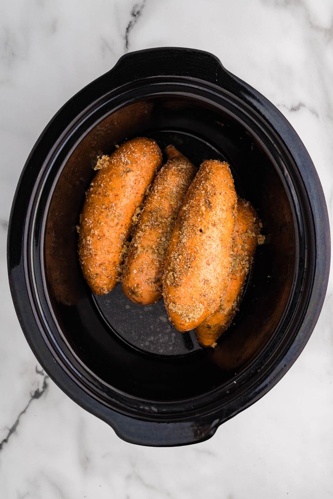 overhead view of four seasoned sweet potatoes in black slow cooker