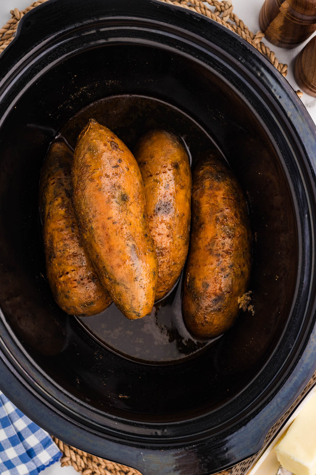 overhead view of four slow cooked sweet potatoes in black slow cooker