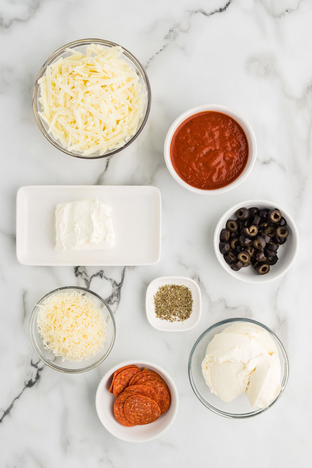 ingredients to include containers of ricotta cheese, cream cheese, mozzarella cheese, Parmesan cheese, pizza sauce, Italian seasoning ,sliced pepperoni and black olives