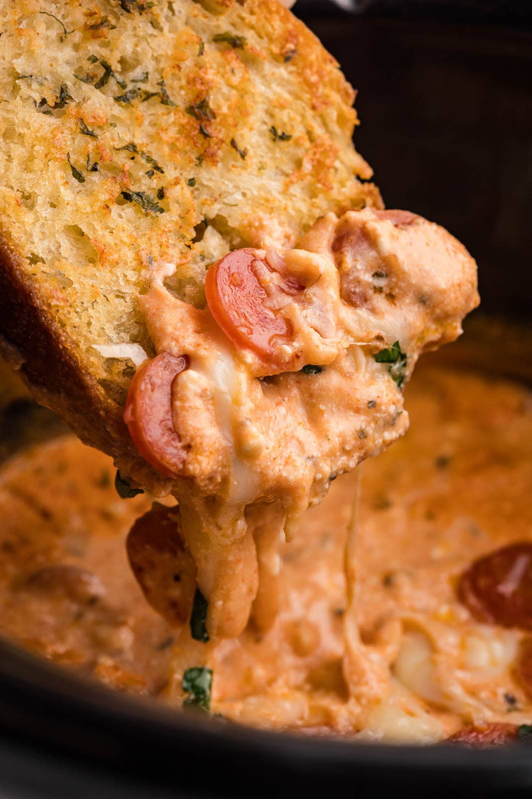 closeup of toasted bread with pizza dip held over slow cooker of pizza dip