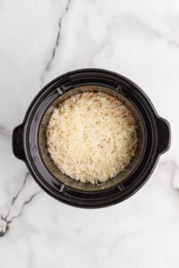 stirred ingredients in black slow cooker with mozzarella and Parmesan cheese on top