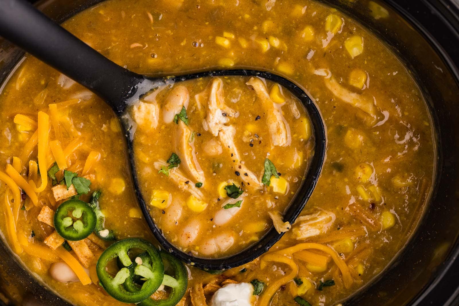 overhead closeup view of black slow cooker containing soup with black ladle inserted