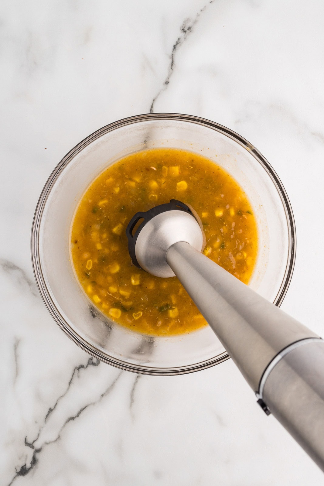 glass bowl containing soup with beans with immersion blender inserted