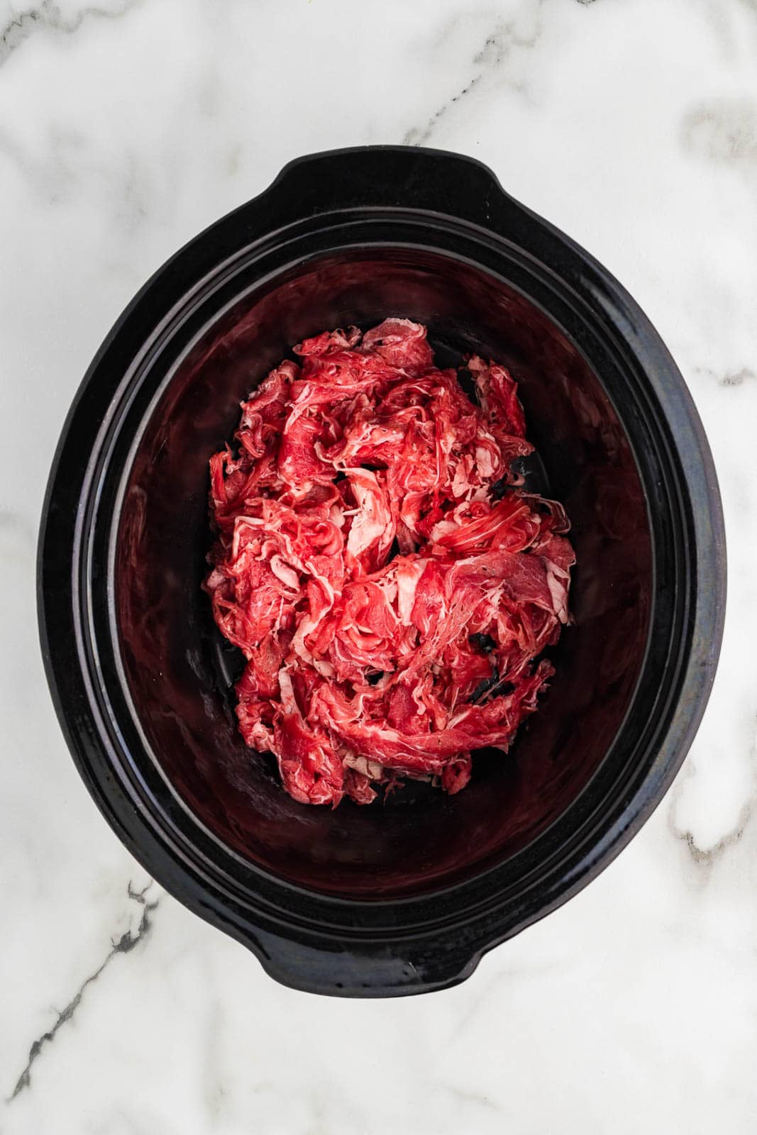 overhead view of black slow cooker with shaved beef steak
