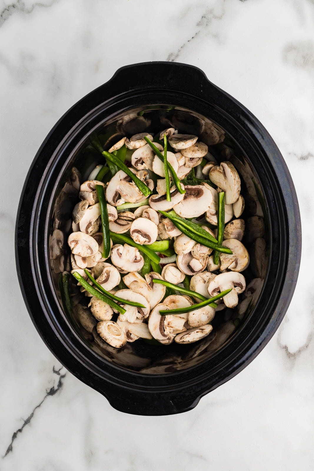 overhead view of black slow cooker with beef, mushrooms, and jalapeno peppers on top