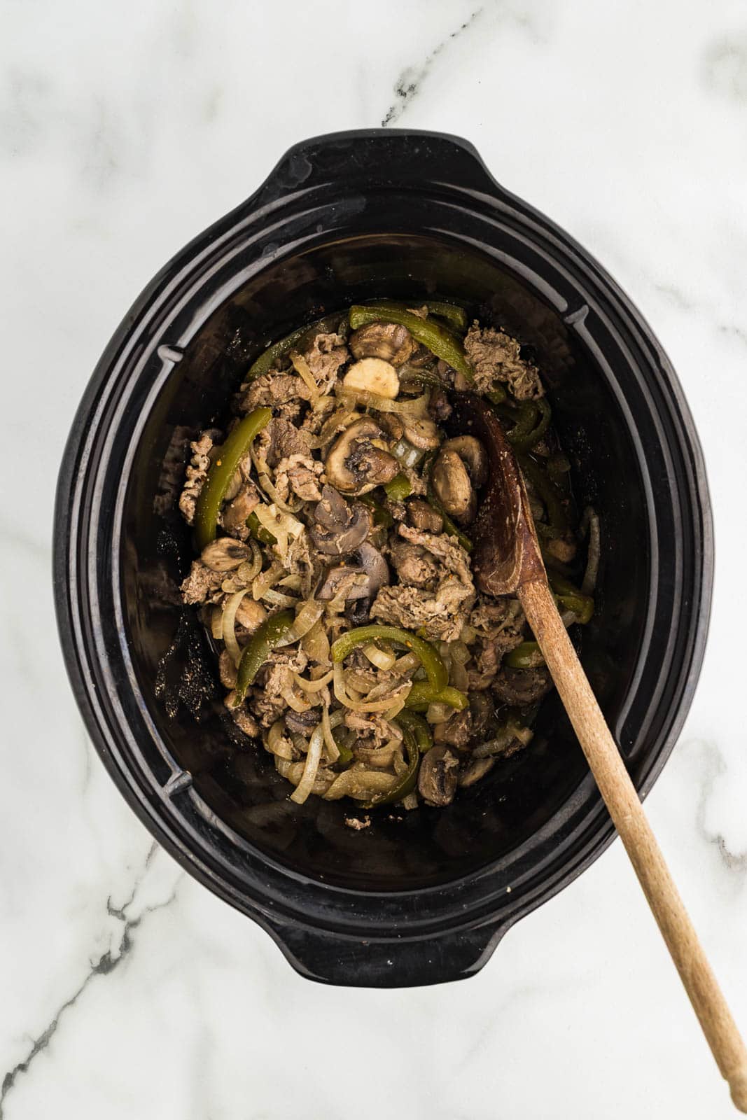 overhead view of slow cooker with cooked beef steak with wooden spoon inserted