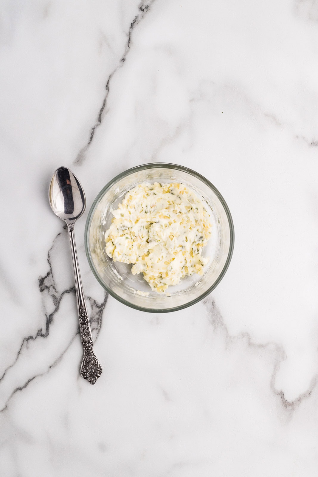small glass bowl butter, garlic, parsley and chives, with spoon on the side