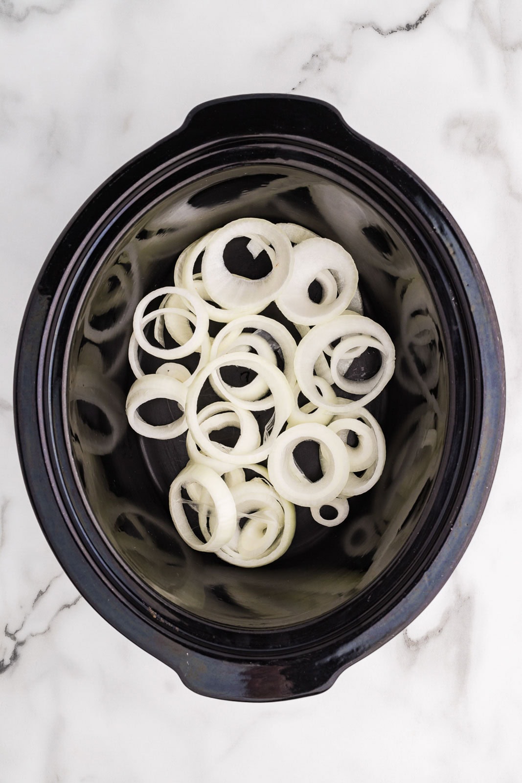 overhead view of black slow cooker with sliced onions on the bottom