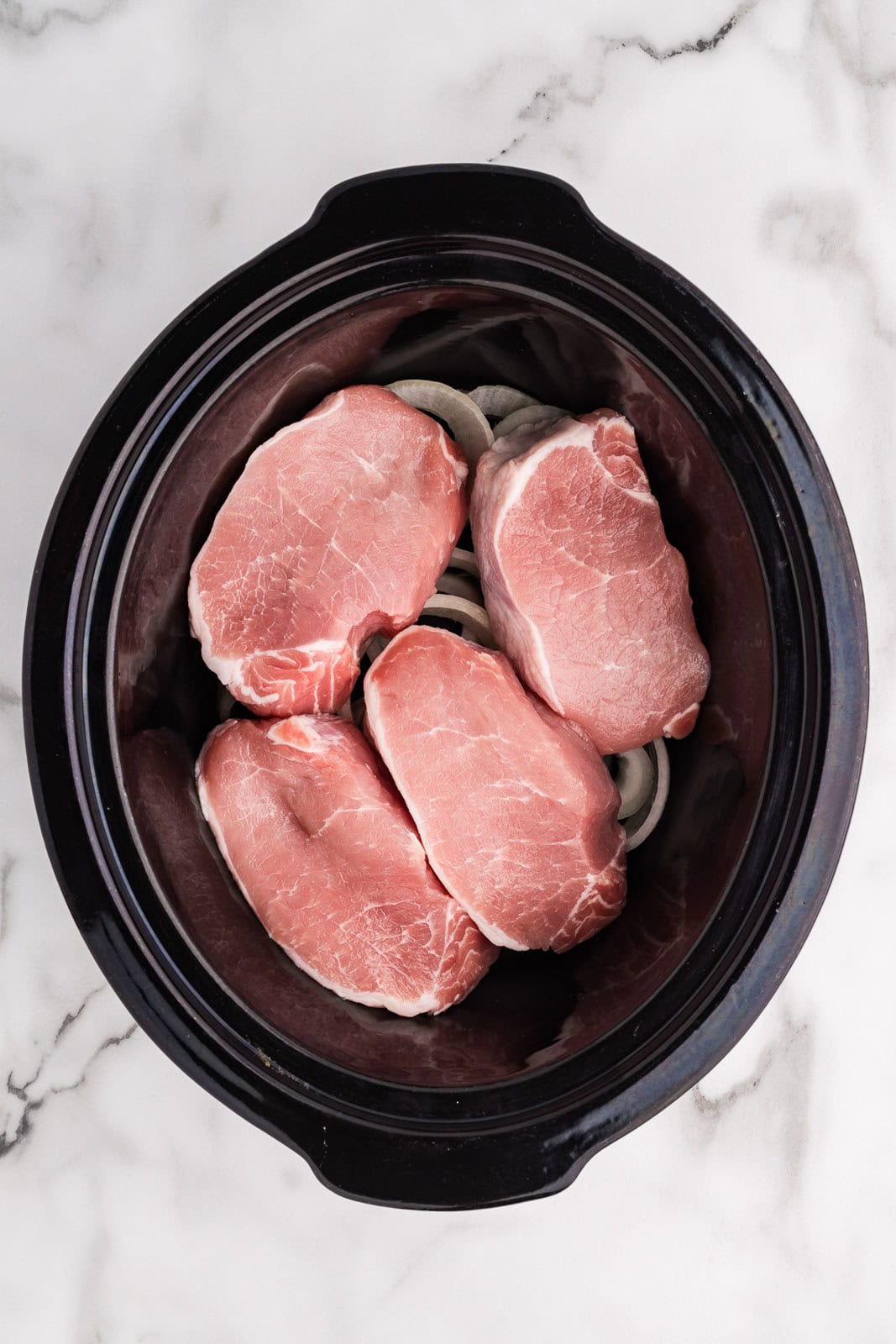 overhead view of black slow cooker with pork chops on top of onions