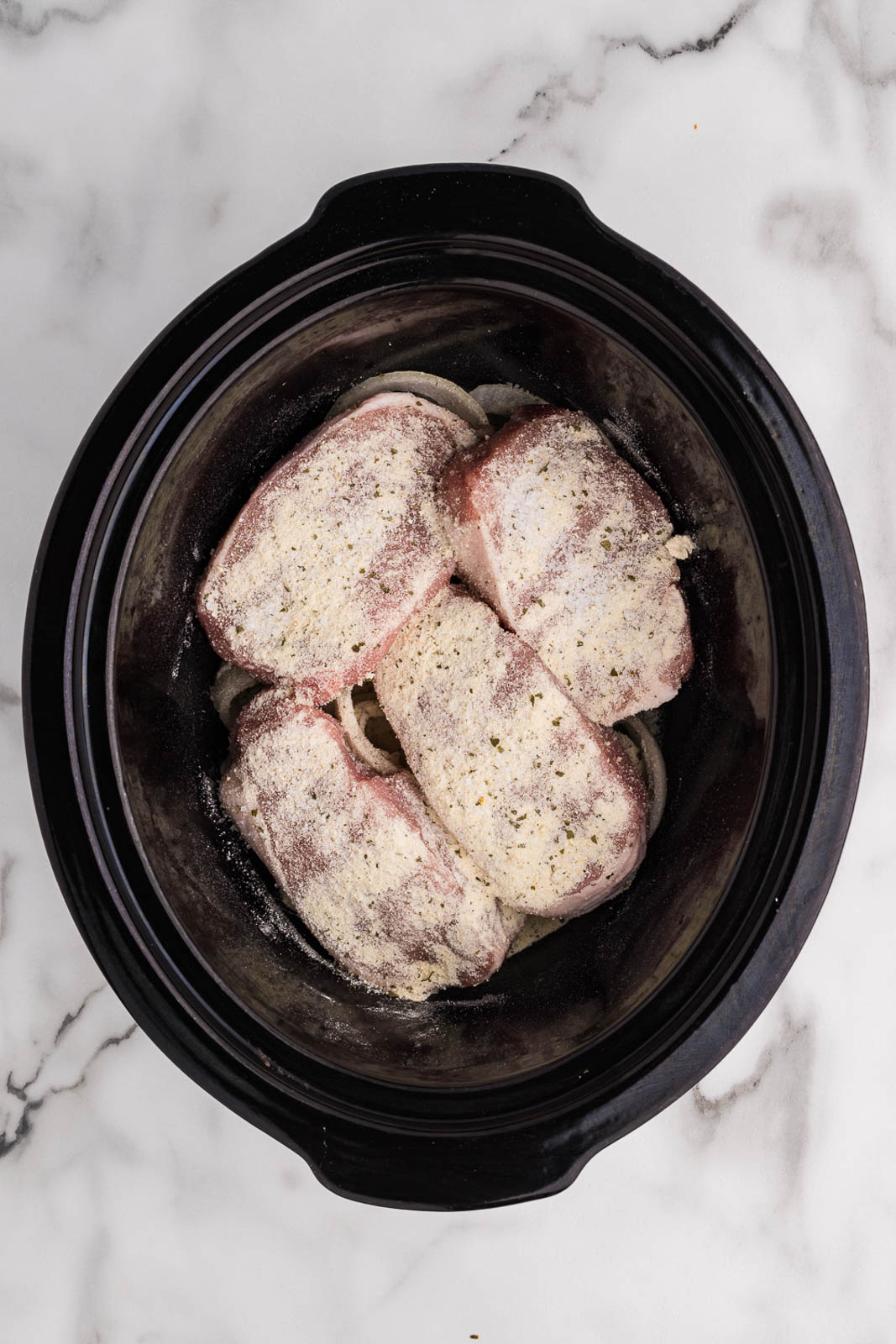 overhead view of sliced onions and pork chops that have been sprinkled with ranch seasoning