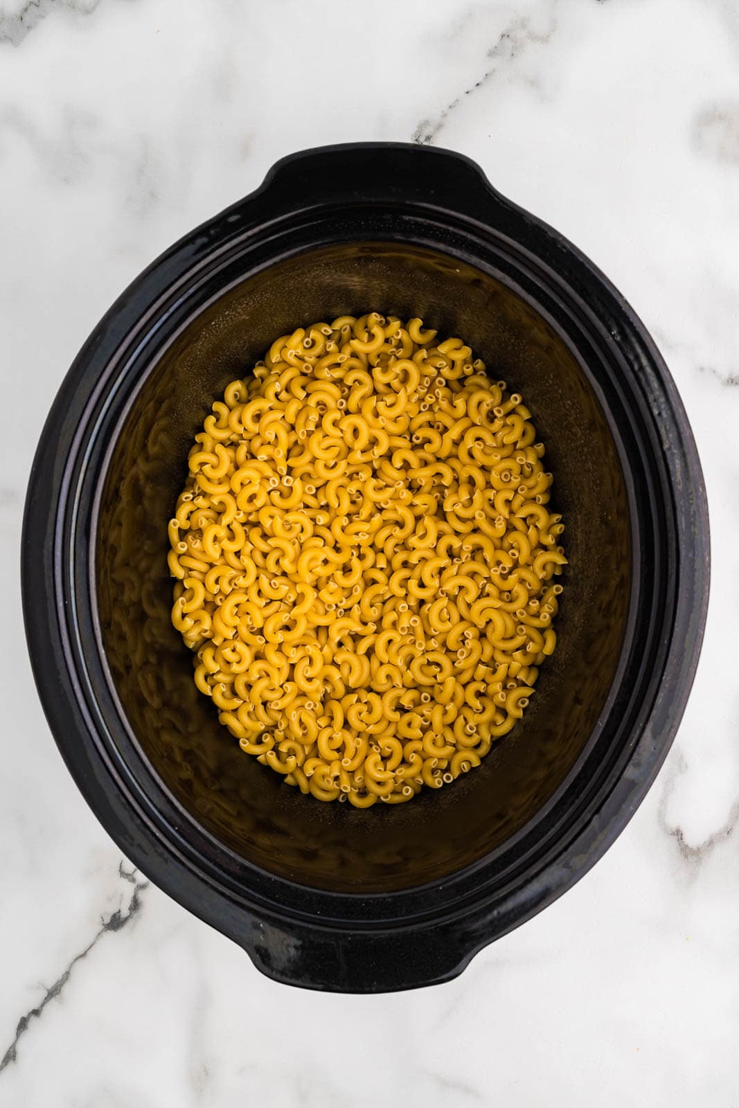 overhead view of black slow cooker with uncooked macaroni