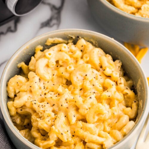 closeup view of two bowls of Mac and cheese with black slow cooker in the background