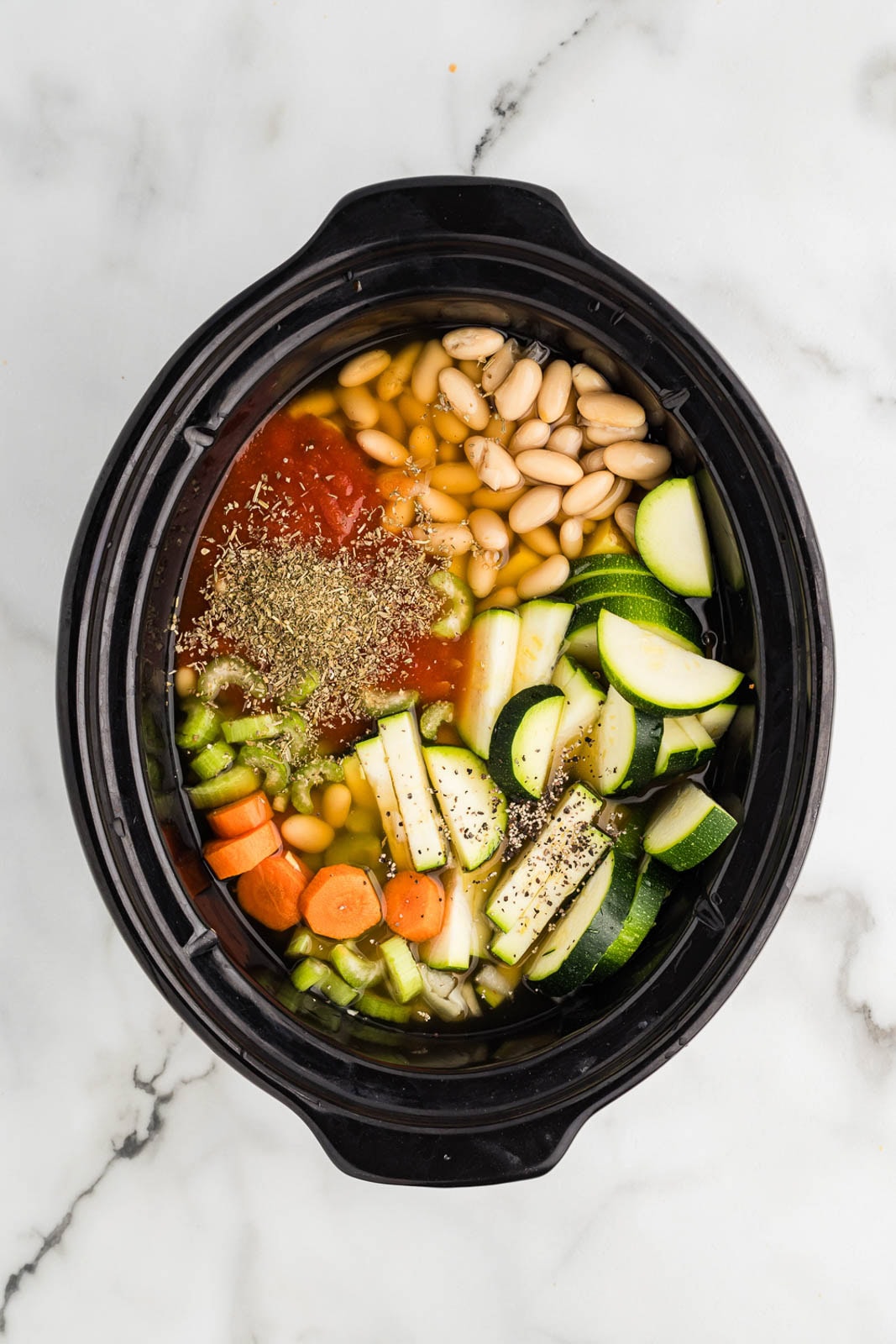 overhead view of black slow cooker with all ingredients except for green beans and peas