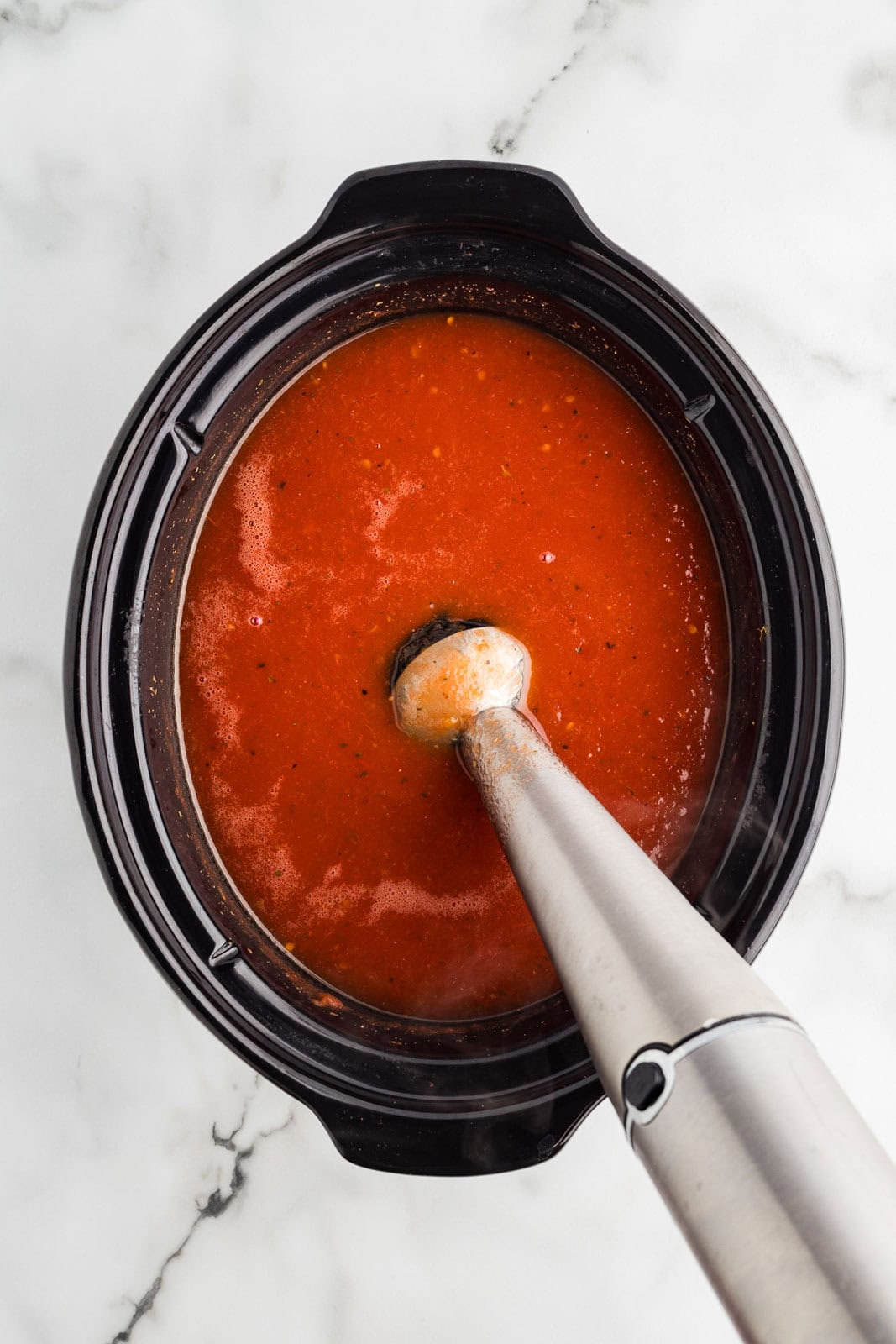 overhead view of black slow Cooker with immersion blender inserted into cooked mixture