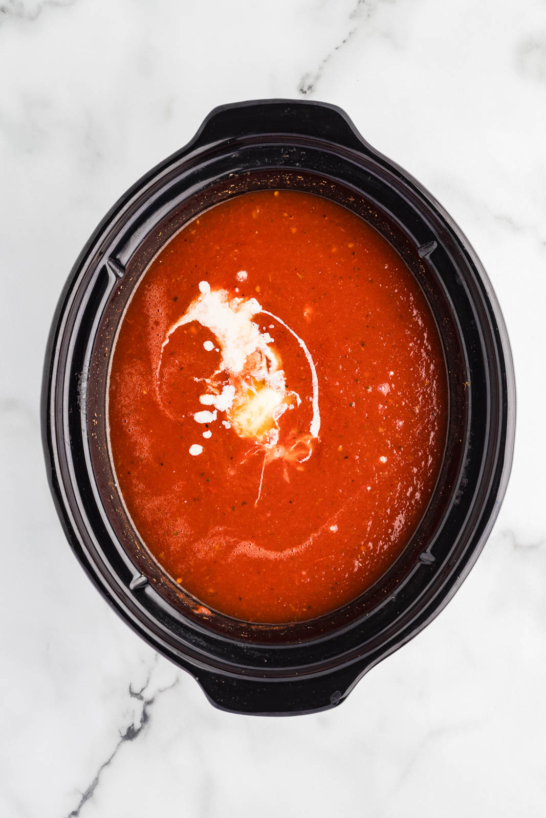 overhead view of black slow Cooker containing cooked mixture with cream, butter, slurry and sugar poured in