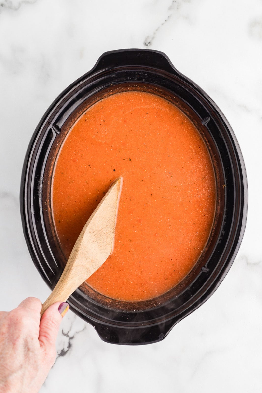 overhead view of black slow Cooker with wooden spoon inserted into mixed soup