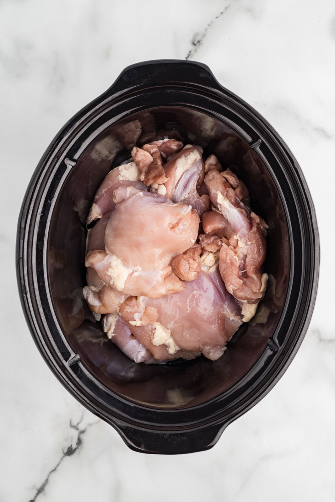 overhead view of black slow Cooker with chicken thighs