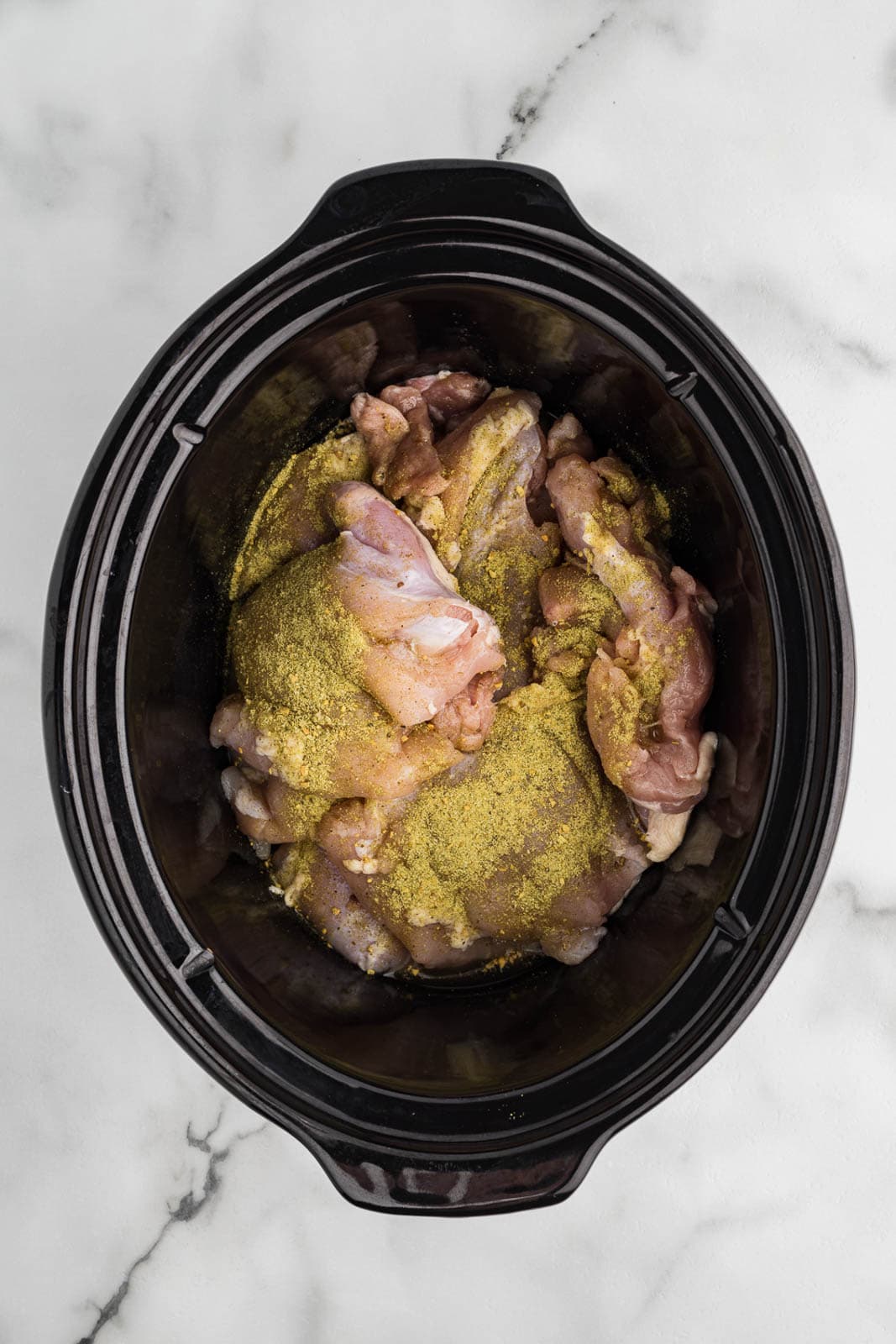 overhead view of black slow Cooker with chicken thighs with seasonings