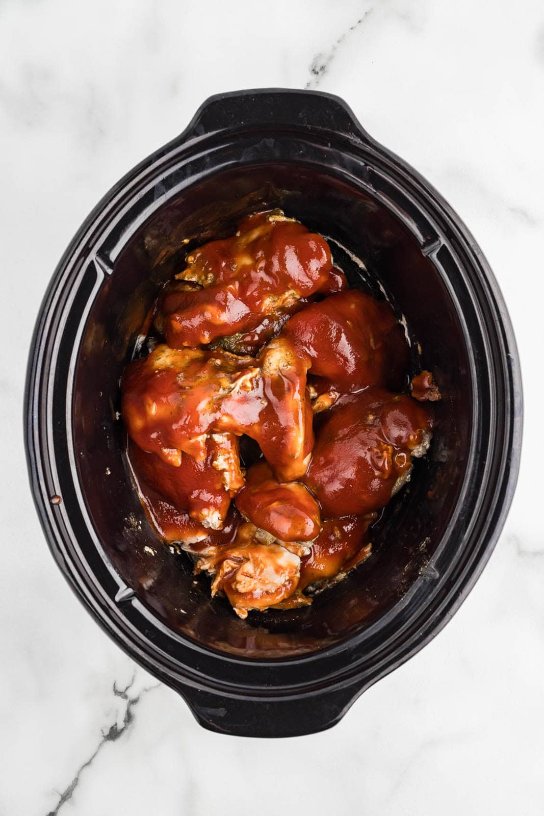overhead view of black slow Cooker with slow cooked chicken thighs with bbq sauce