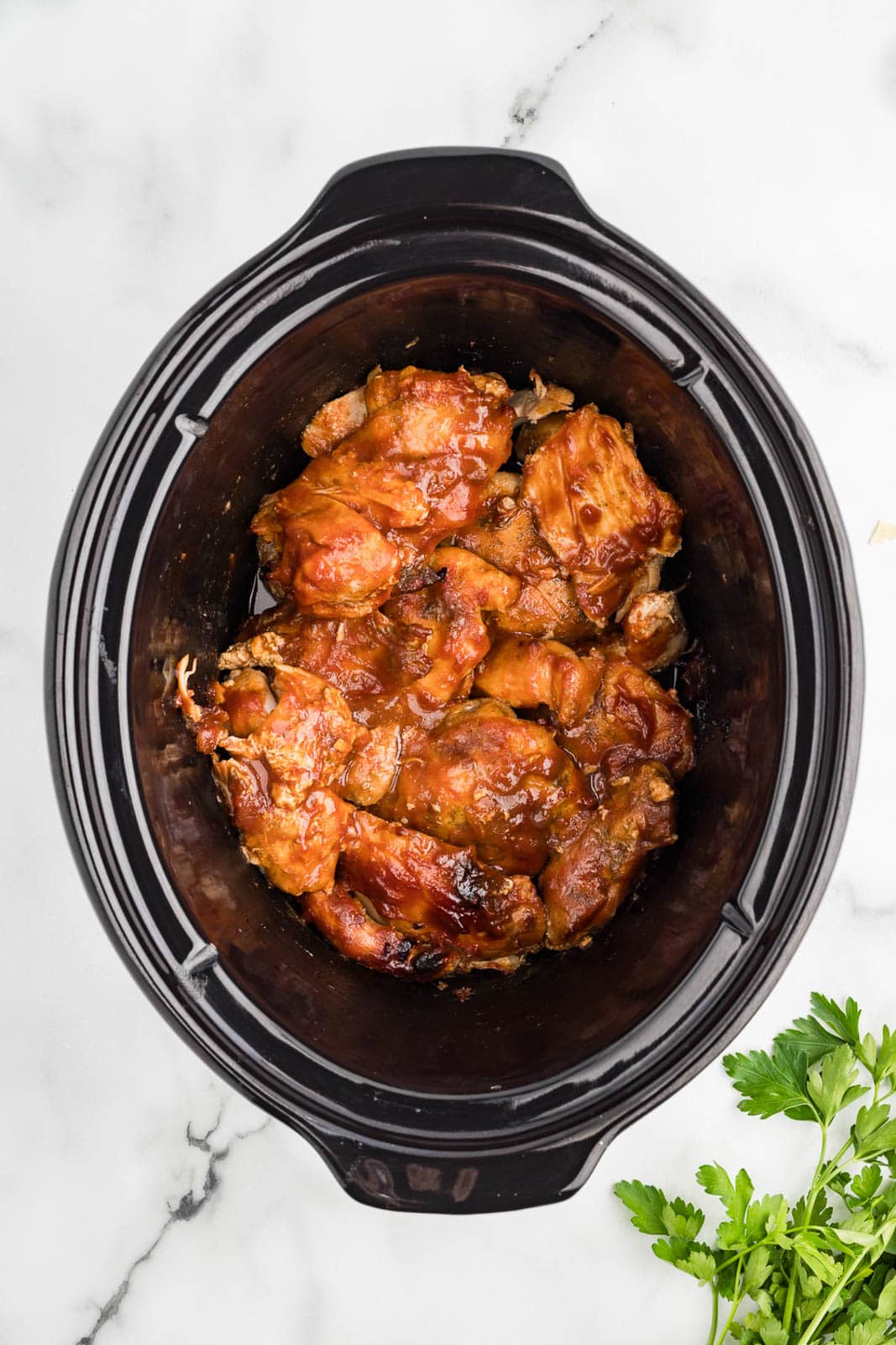 overhead view of black slow Cooker containing slow cooked bbq chicken thighs