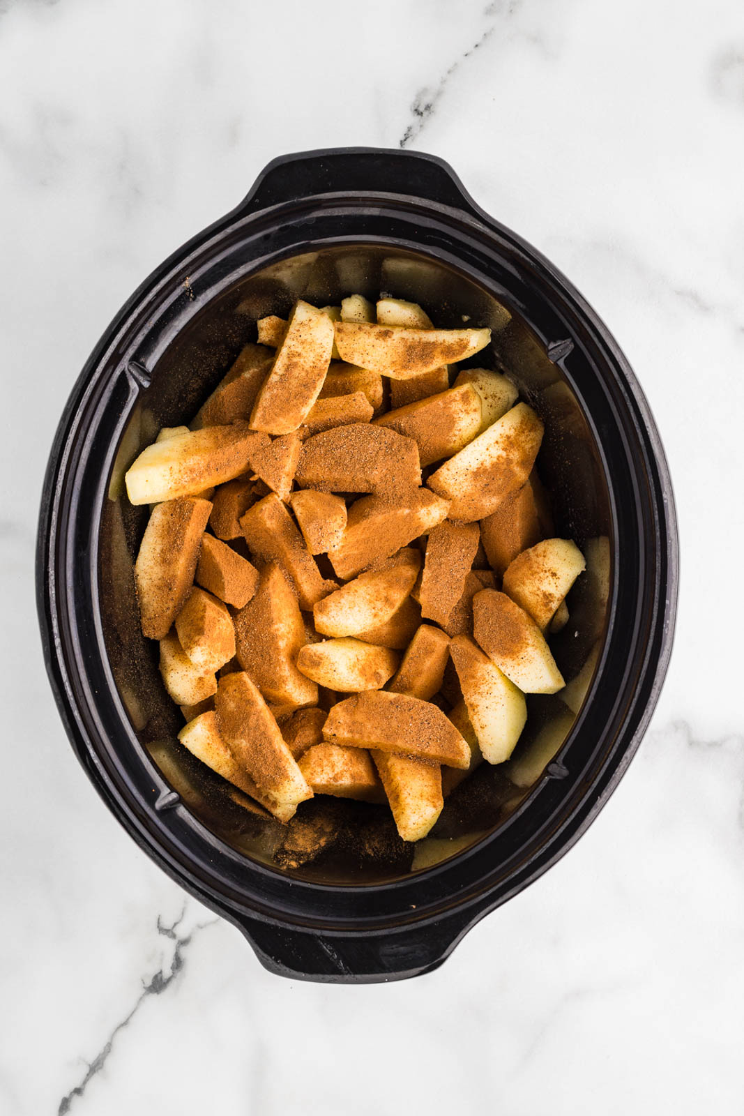 overhead view of black slow Cooker with sliced apples and apple juice with maple syrup and dry ingredients added