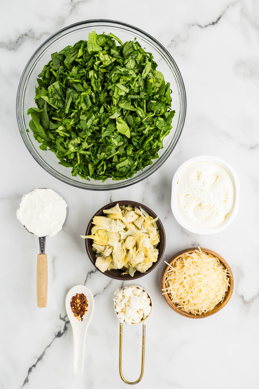 ingredients to include containers of chopped baby spinach, quartered artichoke hearts, whipped cream cheese, sour cream, shredded Parmesan cheese, goat cheese and red pepper flakes