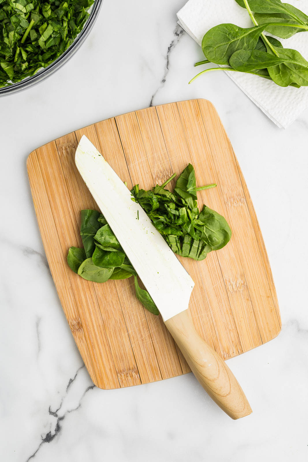 wooden cutting board with chopped baby spinach and knife, with bowl of spinach in background